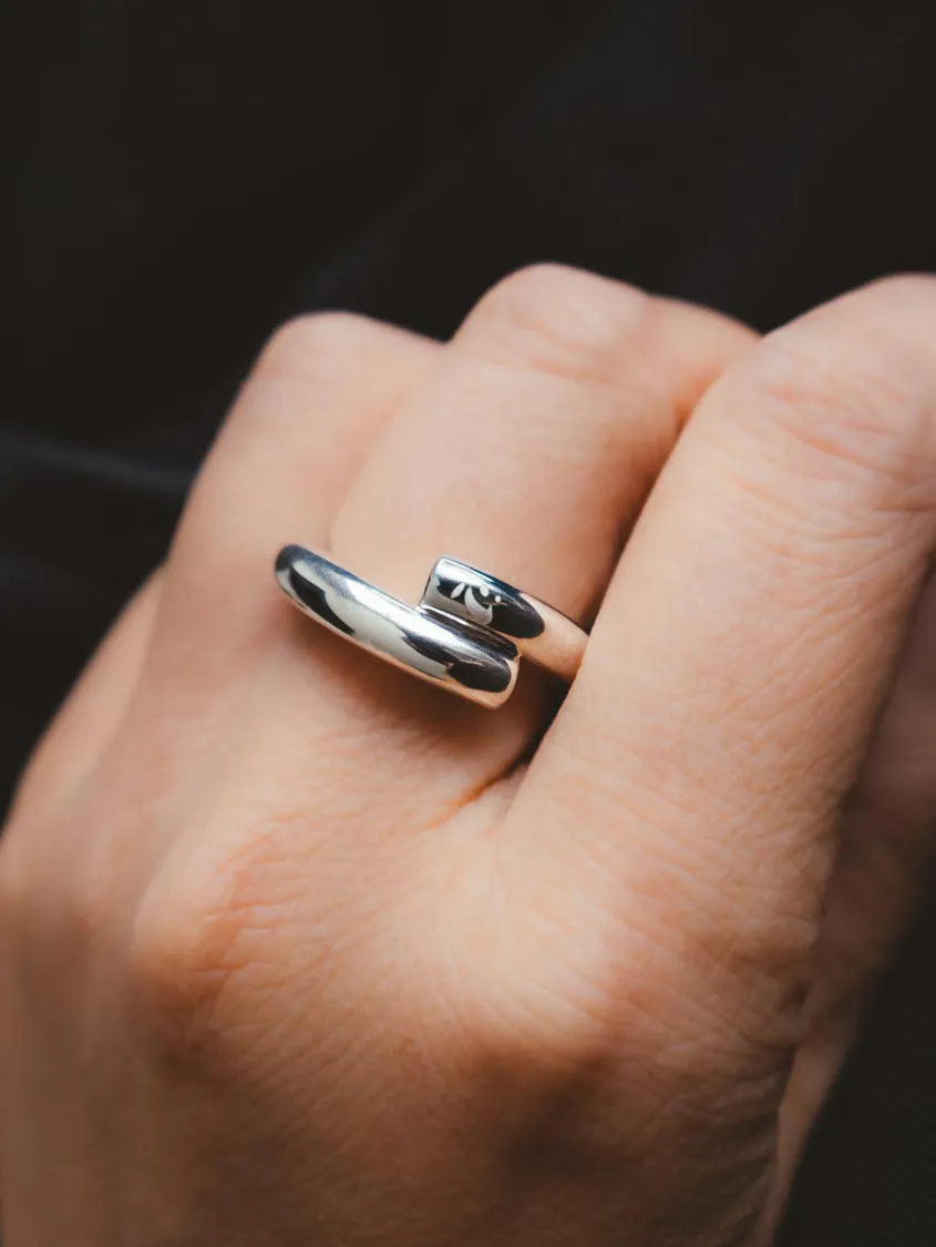 A close-up of a hand wearing a polished silver wrap ring with a small rectangular inlay featuring the number 13.