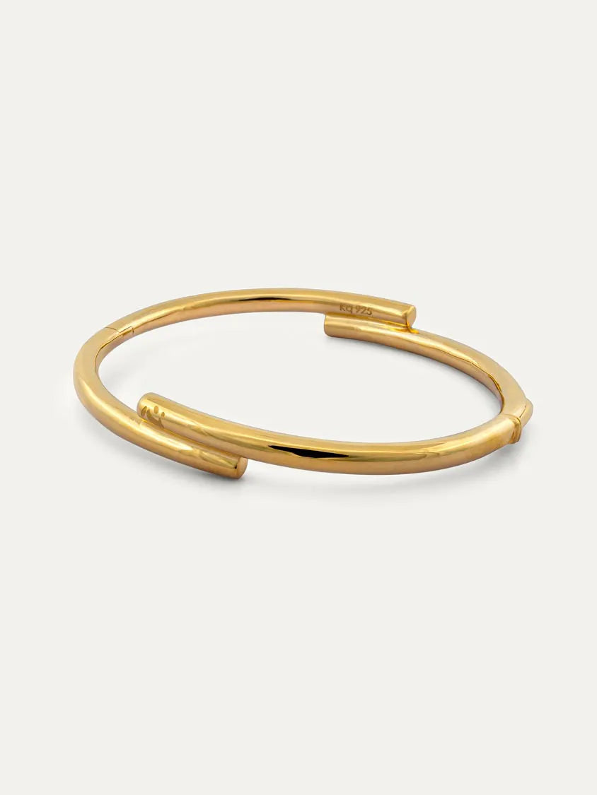 A polished gold open cuff bangle bracelet with a clasp and with engraved Chinese character 心, displayed on a clean off-white background.