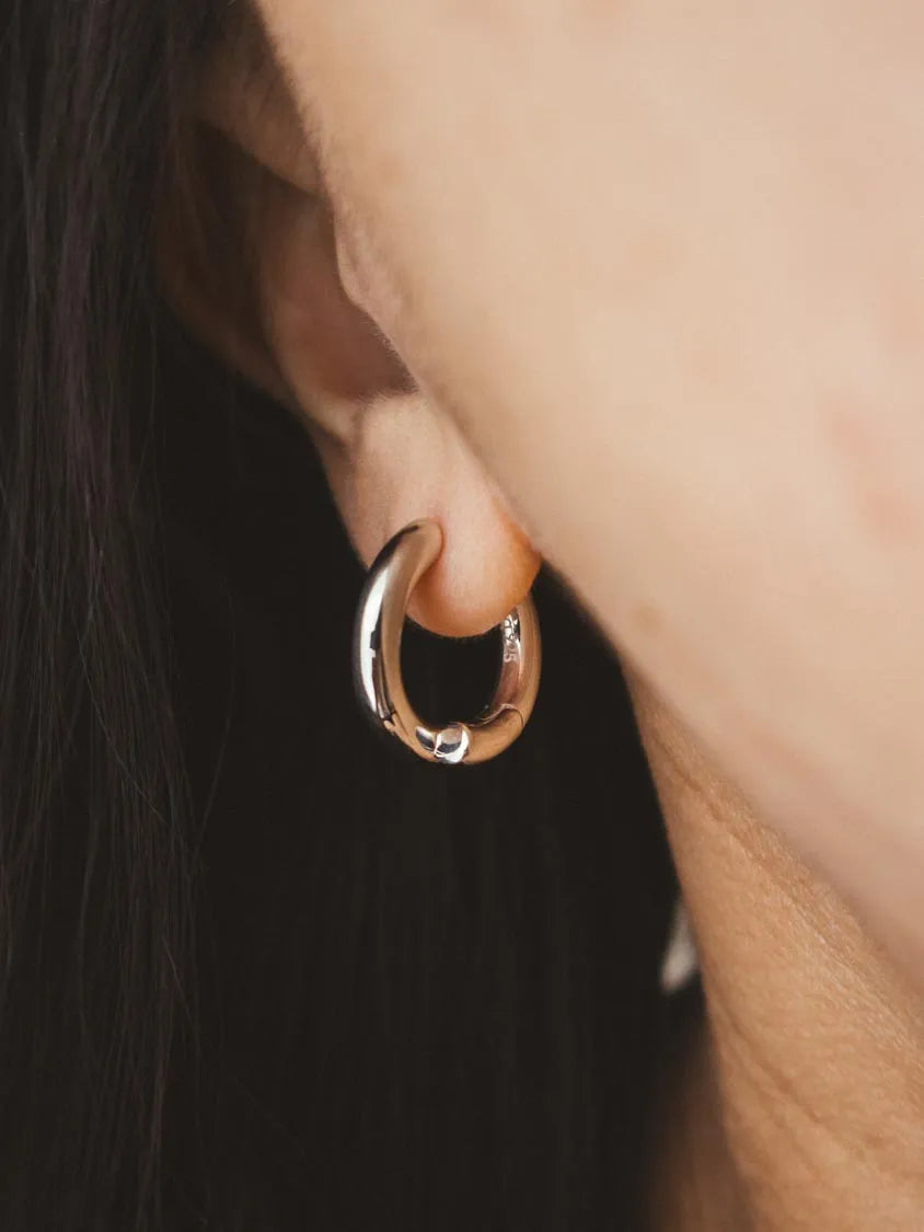 A close-up shot of a person's ear wearing a polished silver-tone hoop earring.