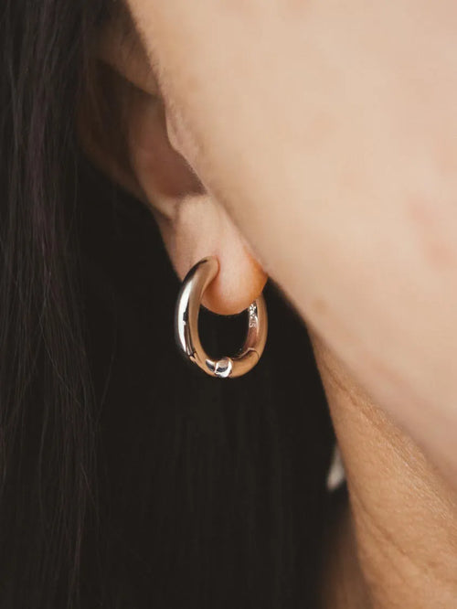 A close-up shot of a person's ear wearing a polished silver-tone hoop earring.