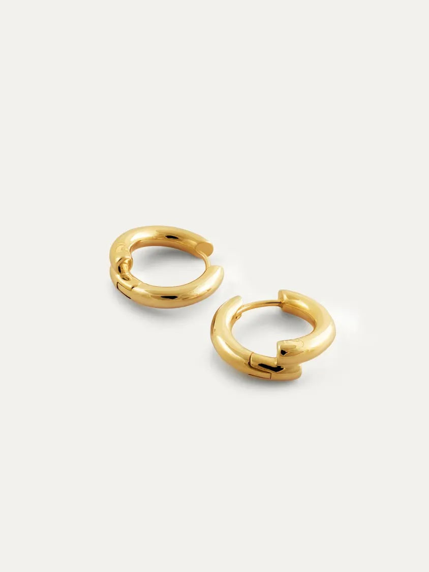 A pair of polished 18k gold vermeil hoop earrings on a light off-white background.