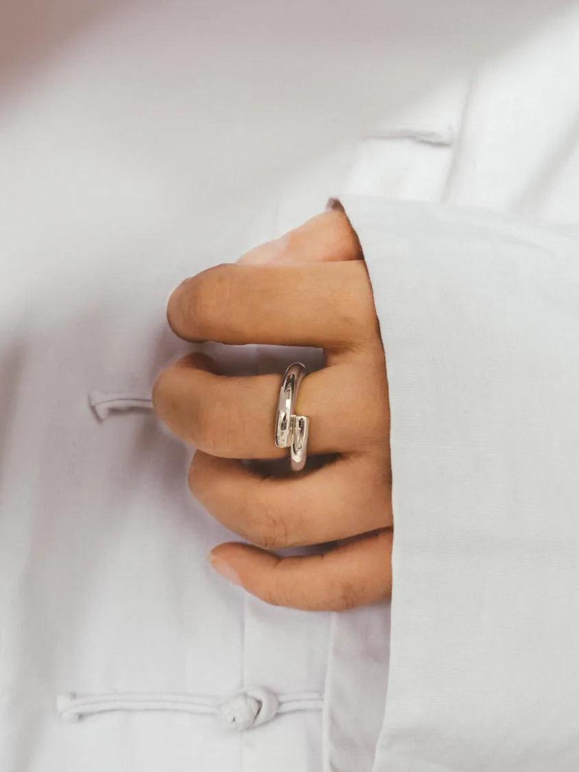 A close-up of a hand wearing a polished Silver ring, resting against a Chinese white traditional-style garment.
