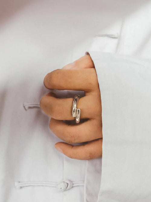 A close-up of a hand wearing a polished Silver ring, resting against a Chinese white traditional-style garment.